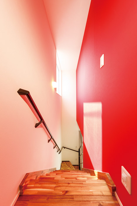 見上げるとモダンアートのような刺激的なイタリアンレッドの壁紙が印象に残る階段室。大きく開いた高窓からの光がほんのり赤く色づいて反射し、まるで異空間を通り抜けるような不思議な感覚に包まれます。階段の踏み面はフローリングと同じアカシア材。階段手摺りはスチール製のシースルーにして、リビングの開放感を損なわないように配慮するとともに、階段とLDKの相互に光を通すことで、家全体を明るくしています。