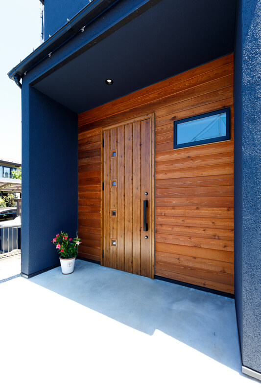木材をあしらった玄関周り。濃紺色の外壁とのコントラストが効いて、モードな外観にアクセントを加えています。アプローチを広く、把手を低めの位置にするなど、家族それぞれの日常の使い勝手にも配慮しています。
