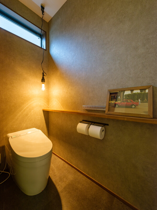 自然光と裸電球のペンダントライトを照明に、雰囲気のあるトイレ。壁のクロスと床のタイルはテイストを揃えて統一感をもたせています。
